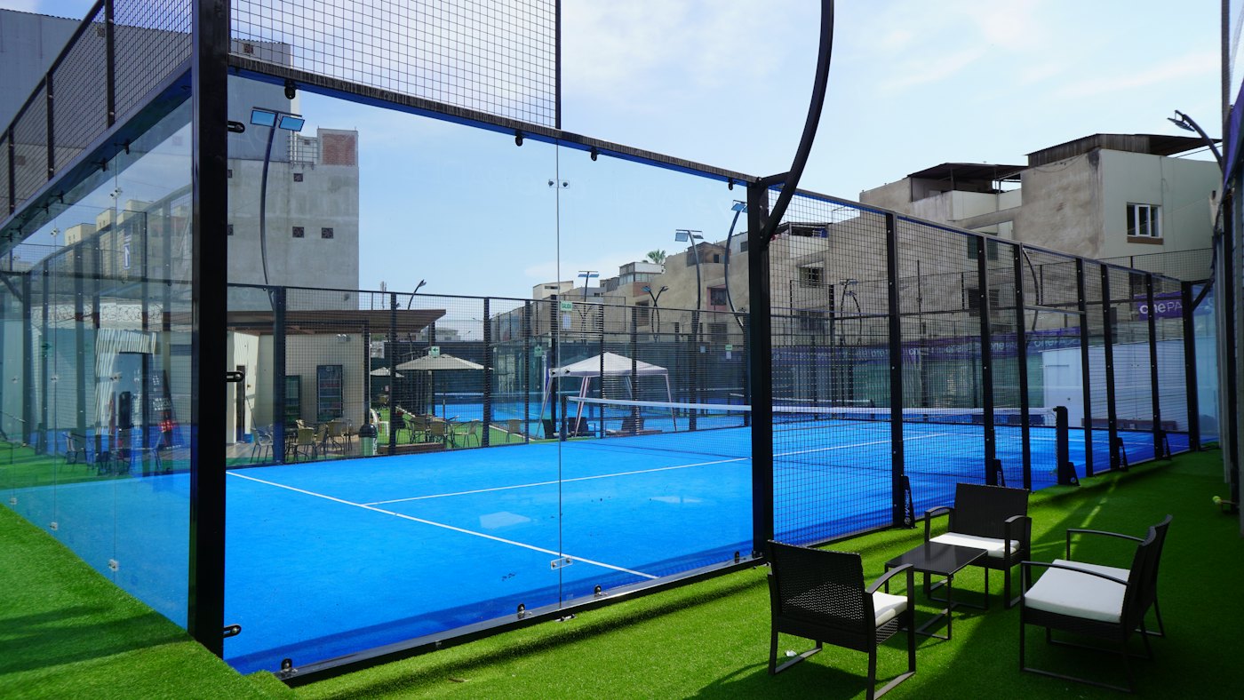A blue padel court with seating beside it