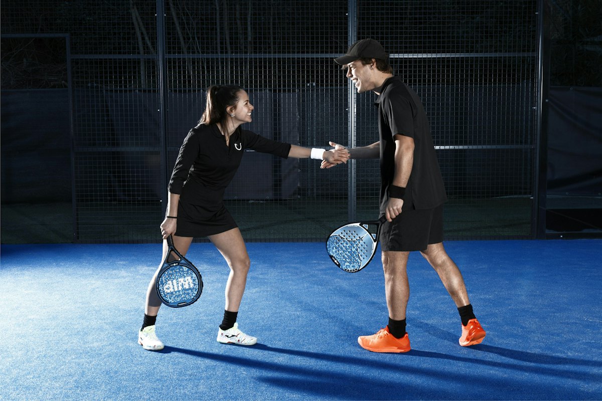 Two padel players shaking hands on a blue court