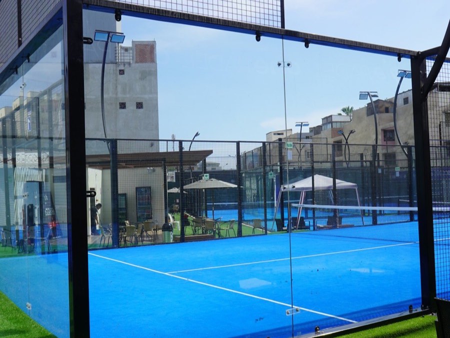 Frameless glass walls around a blue padel court